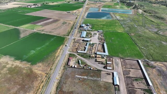 Aerial rural town traffic valley agriculture fields Utah. Farming community agricultural economy. Spring summer weather mountain valley green agriculture field. Homes, barns and buildings.