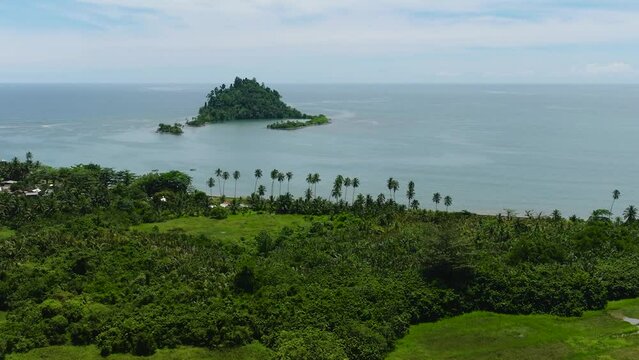 Aerial view of tropical island with green trees under clear sky and clouds. Davao Oriental, Philippines.