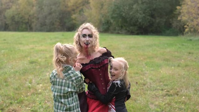 The family celebrates Halloween. Mom in the form of a vampire, girls in the form of a cheerleader and a pumpkin. Mom plays with her daughters. Horizontal video
