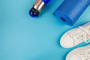 The concept of sports accessories. Photo of blue dumbbells and a blue exercise mat, white sneakers and other sports equipment.