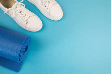 The concept of sports accessories. Photo of blue dumbbells and a blue exercise mat, white sneakers and other sports equipment.
