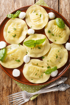 Homemade Italian dumplings pasta cappellacci with mozzarella and herbs close-up in a plate on the table. Vertical top view from above