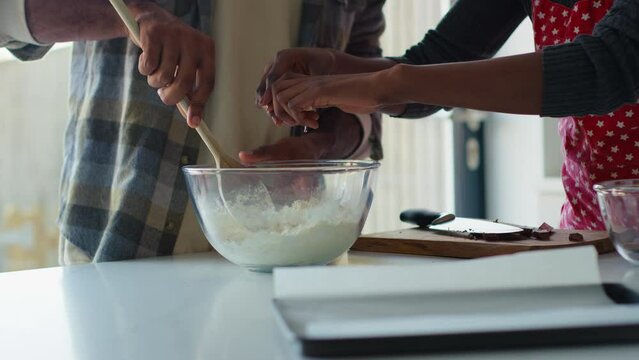 Close up of couple at home in kitchen preparing ingredients to bake cake breaking egg into bowl - shot in slow motion