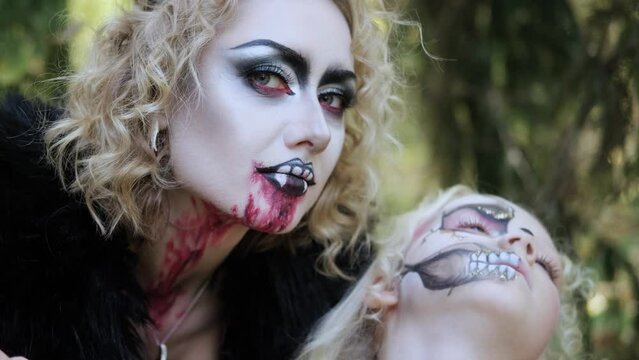 A woman in the form of a vampire or a sorceress bites a princess girl in fairy-tale makeup and medieval dress. Image for Halloween. Horizontal video