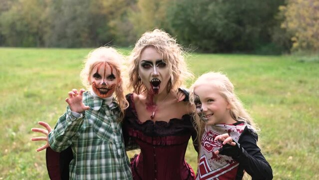 The family celebrates Halloween. Mom in the form of a vampire, girls in the form of a cheerleader and a pumpkin. Mom plays with her daughters. Horizontal video