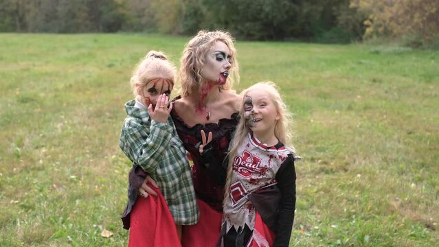 The family celebrates Halloween. Mom in the form of a vampire, girls in the form of a cheerleader and a pumpkin. Mom plays with her daughters. Horizontal video