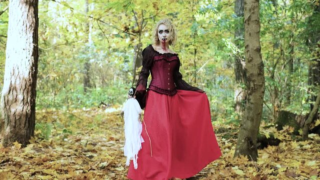 A woman in the form of a vampire or a witch holds a doll in the form of death in her hands. Blood trickles down the vampire's chin. Horizontal video