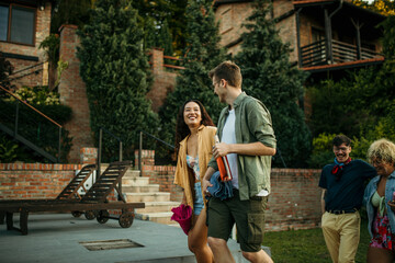 Obraz premium Group of friends walking towards the pool, holding a vine, and having a backyard party.