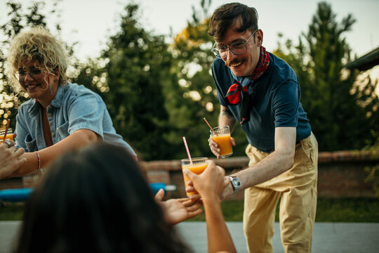 The male host serves juices and drinks to his friends around the pool. - Powered by Adobe