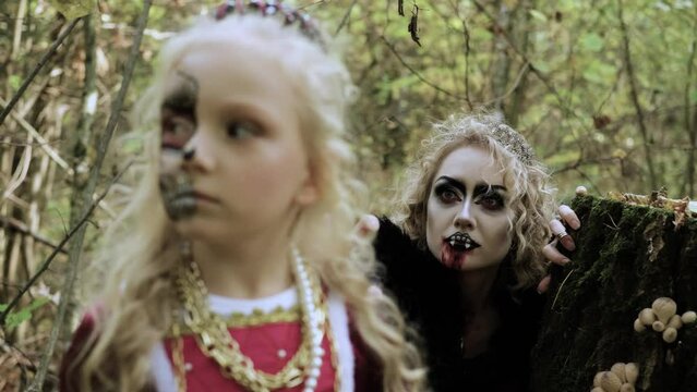 A woman in the form of a vampire or a sorceress is about to bite a princess girl in fairy-tale makeup and medieval dress. The witch is watching the girl. Image for Halloween. Mother and daughter. 