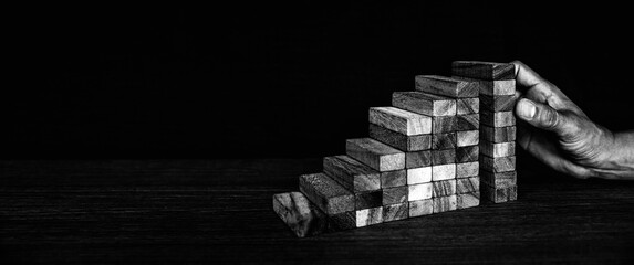 Hand placing wooden block tower stack in pyramid stair step with caution to prevent collapse or...