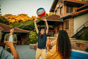 A group of people play a lively game of volleyball by the pool, jumping and diving to keep the ball...