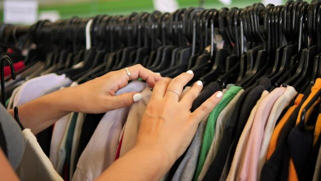 Young woman choosing t-shirt from hanger in second hand clothing store, 4K consumerism reduse reuse recycle concept footage. Chiang Mai, Thailand.
