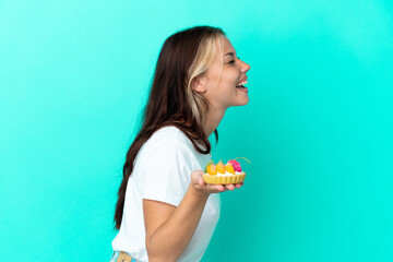 Young Russian woman holding a fruit sweet isolated on blue background laughing in lateral position