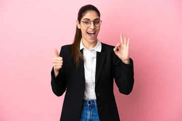 Young caucasian business woman isolated on pink background showing ok sign and thumb up gesture