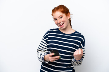 Young reddish woman isolated on white background with phone in victory position