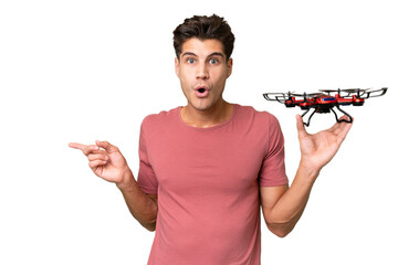 Young caucasian man holding a drone over isolated background surprised and pointing side