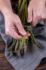 Man peeling green asparagus. Wooden background. Men's hands and organic fresh asparagus