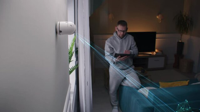 Man sets up security camera with AI recognition at home using digital tablet. 3D render of modern CCTV camera rotating, scanning objects in room with laser beams. VFX animation. Surveillance system.