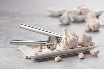 Garlic and garlic press on a grey table.