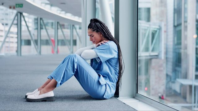 Woman, doctor and headache in mistake, stress or burnout sitting on floor in the hospital building. Frustrated or sad female person or medical healthcare nurse crying in grief, loss or failed surgery