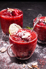 Blended strawberry shake smoothie with whole strawberries, ice and lemon in glasses on black background.