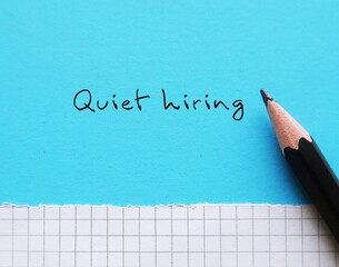 Pencil writing on blue background Quiet hiring - a term describes businesses adding new skills and filling position gaps without new full- time employees