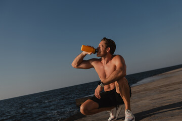 Fototapeta na wymiar Confident male athlete drinking water while resting after morning training outdoors