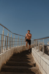 Confident male athlete running down the stairs outdoors with a blue sky on background