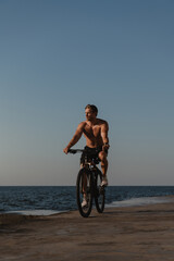 Fototapeta na wymiar Handsome young shirtless man enjoying summer morning while cycling seaside
