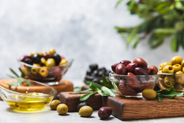 A set of green, red and black olives on a light marble background. Various types of olives in bowls and fresh olive leaves. Vegan. Olive fruits. Place for text. Copy space.
