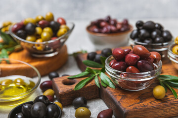 A set of green, red and black olives on a light marble background. Various types of olives in bowls and fresh olive leaves. Vegan. Olive fruits. Place for text. Copy space.
