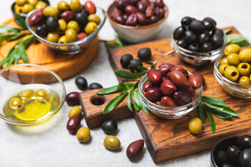 A set of green, red and black olives on a light marble background. Various types of olives in bowls and fresh olive leaves. Vegan. Olive fruits. Place for text. Copy space.