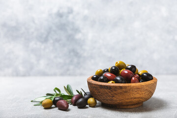 A set of green, red and black olives on a light marble background. Various types of olives in bowls and fresh olive leaves. Vegan. Olive fruits. Place for text. Copy space.
