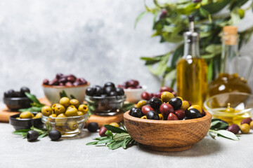 Obraz na płótnie Canvas A set of green, red and black olives on a light marble background. Various types of olives in bowls and fresh olive leaves. Vegan. Olive fruits. Place for text. Copy space.