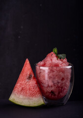 Watermelon sorbet in glass and piece of fresh ripe watermelon on black background. Summer refreshing dessert. Front view.
