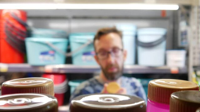 Close-up of many plastic detergent bottles on a store shelf and a male buyer takes one