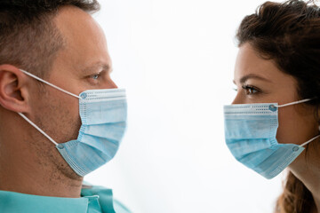 Portrait of two young fearful uneasy people standing face-to-face to each other while wearing protective masks.