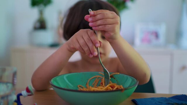 Closeup small boy eating pasta noodles, twisting and turning spaghetti meal with fork