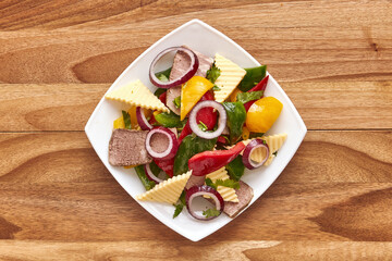 White plate with salad of meat, cheese, bell pepper, red onion and herbs on the wooden table. Top view, flat lay