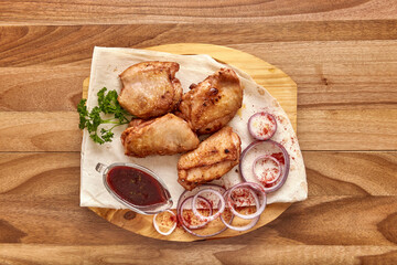 Fried chicken meat with red onion rings, sauce and pita bread on the wooden board on the wooden table, flat lay top view