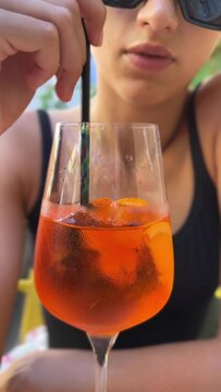 A gorgeous, young girl is drinking Aperol on the restaurant's outdoor patio.
