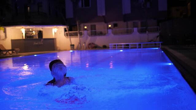 Cute baby boy jumping water at illuminated swimming pool playing with father enjoy summer vacation