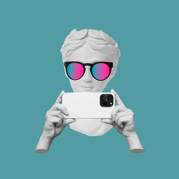 Antique statue's head in sunglasses holding mobile phone with photo camera in hands taking picture on color background. 3d trendy creative collage in magazine style. Contemporary art. Modern design