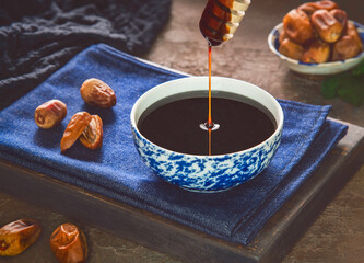 Healthy date syrup with whole and dry pitted dates. Delicious date syrup flows from a wooden honey...