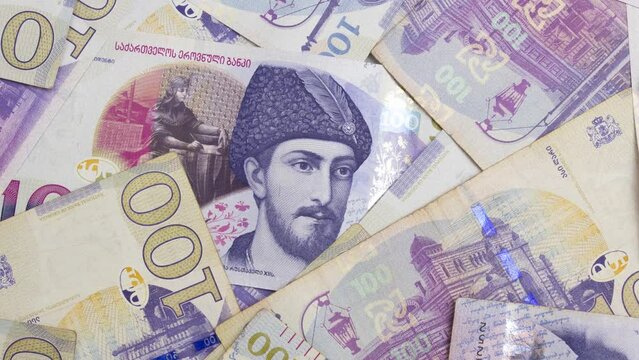 4K video. 100 GEL of Georgia. One hundred lari. Georgian paper banknotes. Male eyes watching from stack of cash money hole. &Mu;an peeks furtively through gap. Concept of mystery, secret, corruption, tax