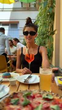 A beautiful young woman is drinking Aperol on the restaurant terrace.