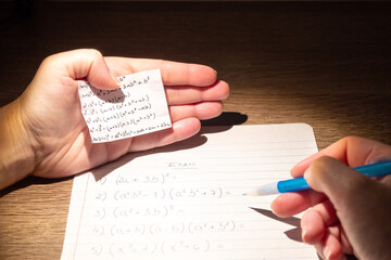 Student using formula math sheet to cheat on test. Hand of university student holding pencil doing math question in examination and cheating with answer piece of paper in hand
