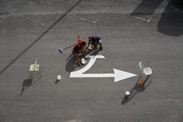Two workers are repairing road sign color along with obstacles for their safety. Top view photo.