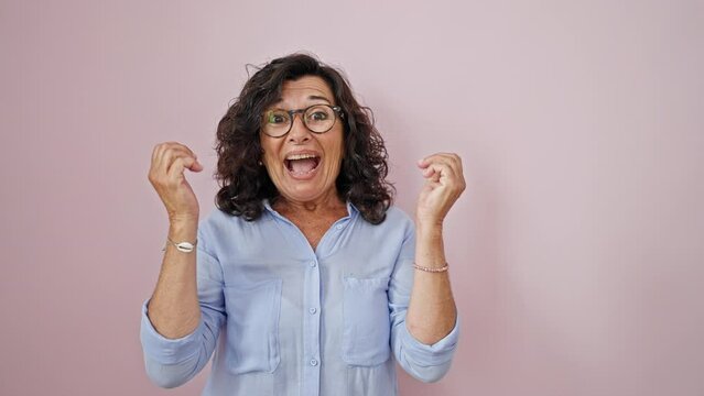 Middle age hispanic woman looking for celebrating over isolated pink background